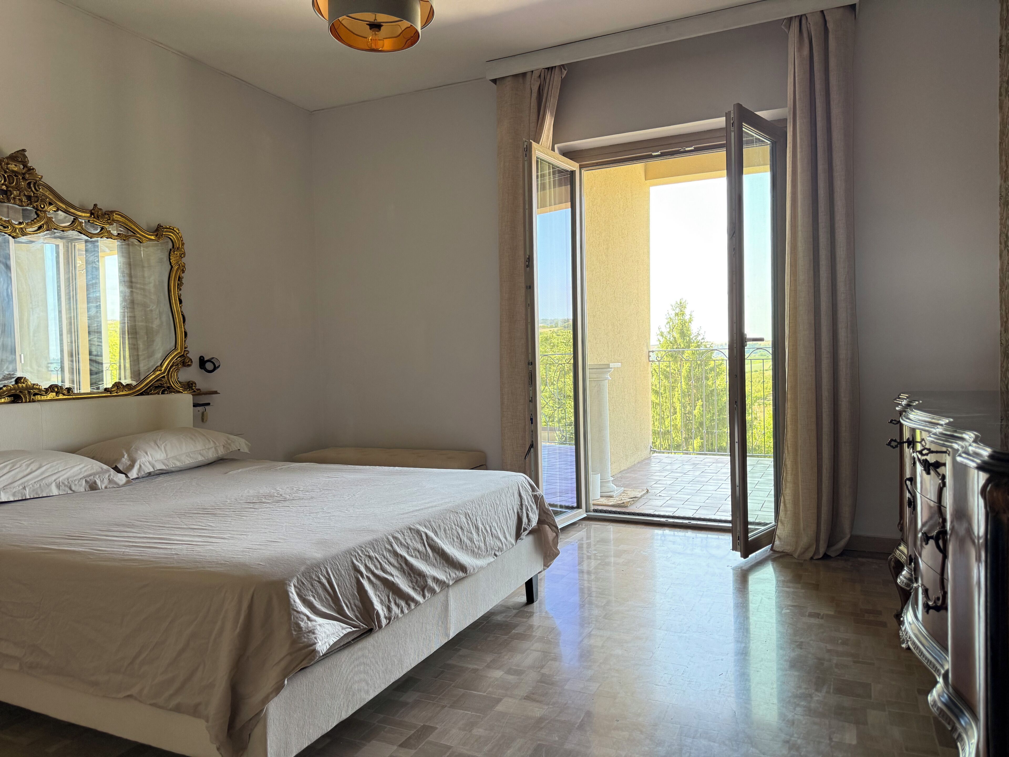 Een slaapkamer met een bed, een grote spiegel, een kaptafel en een balkon met uitzicht.