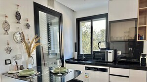 Una cucina moderna con un tavolo da pranzo in vetro, sgabelli da bar neri, un forno integrato e una finestra vista alberi.
