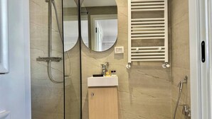 Un bagno moderno con cabina doccia in vetro, mobile lavabo in legno, porta asciugamani e water.