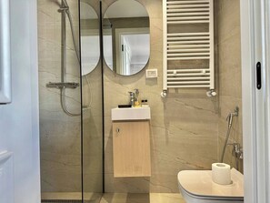 Ein modernes Badezimmer mit einer Duschkabine aus Glas, einem Holzkosmetikschrank, einem Handtuchhalter und einer Toilette.