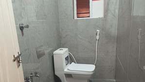 A small bathroom with a toilet, a window with red blinds, a shower, and a blue bucket. - Hotel Homestay Bhimavaram (Bhimavaram)