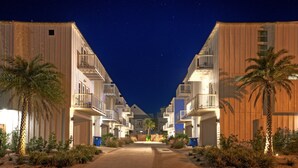 A row of beachfront hotels with balconies, palm trees, and a clear night sky. - Steps to Beach • Pool + Fire Pit + Golf Cart Boardwalk Access | Southern Cross (Port Aransas)