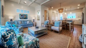 A spacious living room with a blue sofa, a coffee table, and a dining area with a table and chairs. - Steps to Beach • Pool + Fire Pit + Golf Cart Boardwalk Access | Southern Cross (Port Aransas)