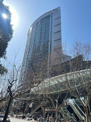 A modern building with a curved glass facade, surrounded by trees and a pedestrian area with escalators. - Shanghai Clivia Hotel (Shanghai)