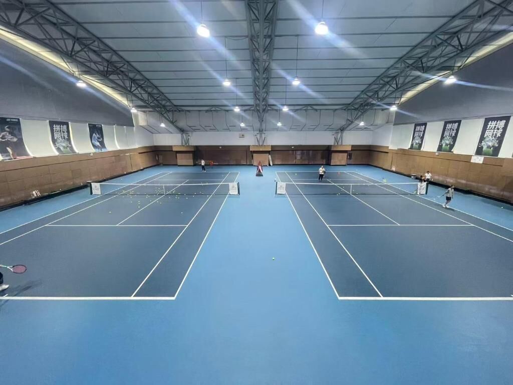 Una gran cancha de tenis cubierta con múltiples canchas, techos altos y banderines en las paredes.
