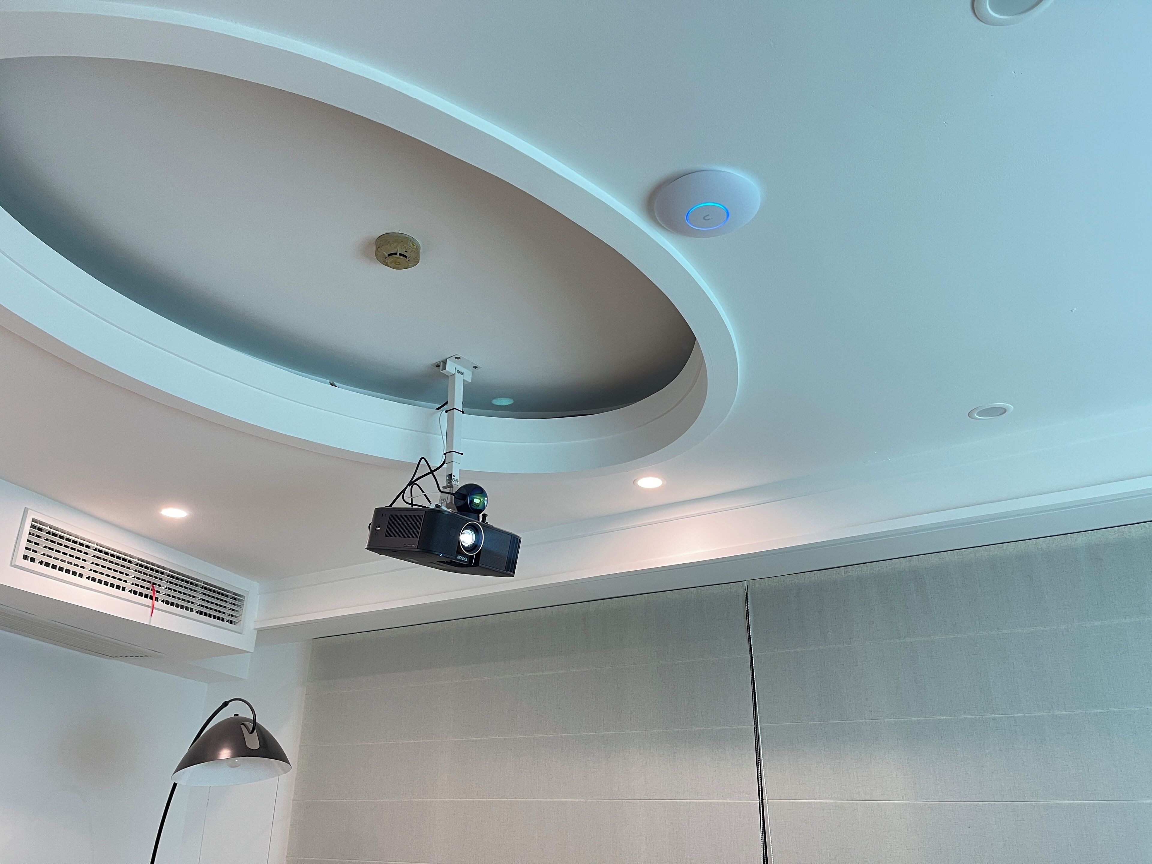 A ceiling with recessed lighting, a smoke detector, and a ceiling-mounted projector.