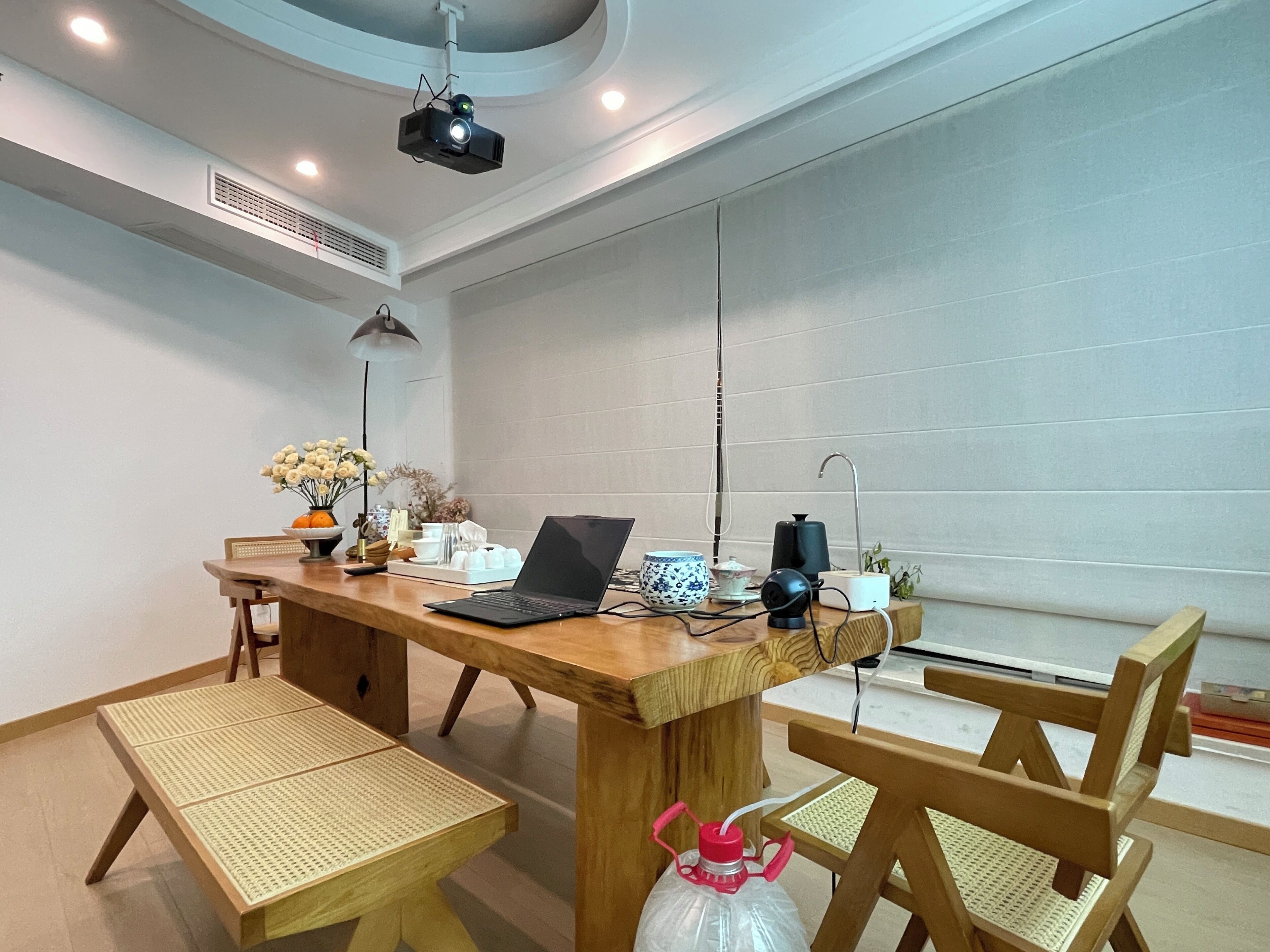 A conference room with a wooden table, chairs, a laptop, a projector, and a small plant.