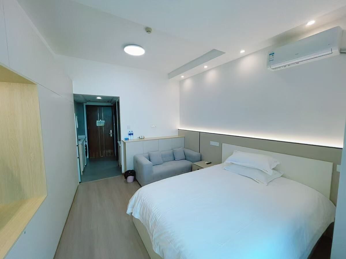 Una habitación de hotel moderna con una cama grande, una mesita de noche, un pequeño sofá y un escritorio con una silla.