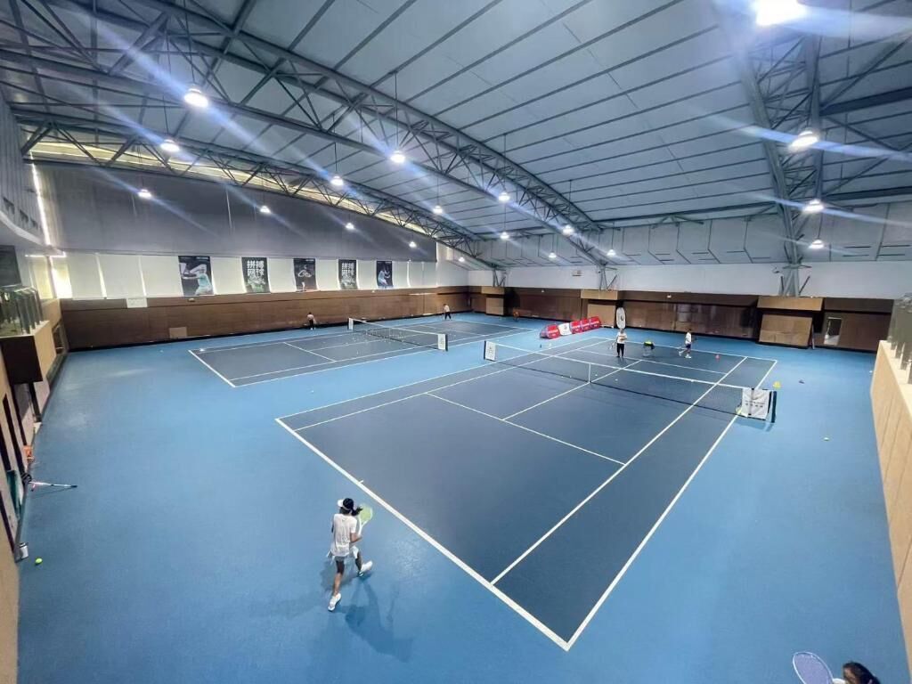 Pista de tenis interior con varias canchas, techo alto e iluminación artificial.