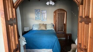 A bedroom with a bed, wooden doorways, a ceiling fan, and two wall-mounted paintings. - Tres Corazones Grand Suite for two (Playas la Misión)