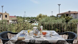 Een tafel gedekt met kopjes, een boek en een koffiepot op een balkon met uitzicht op gebouwen en bomen.