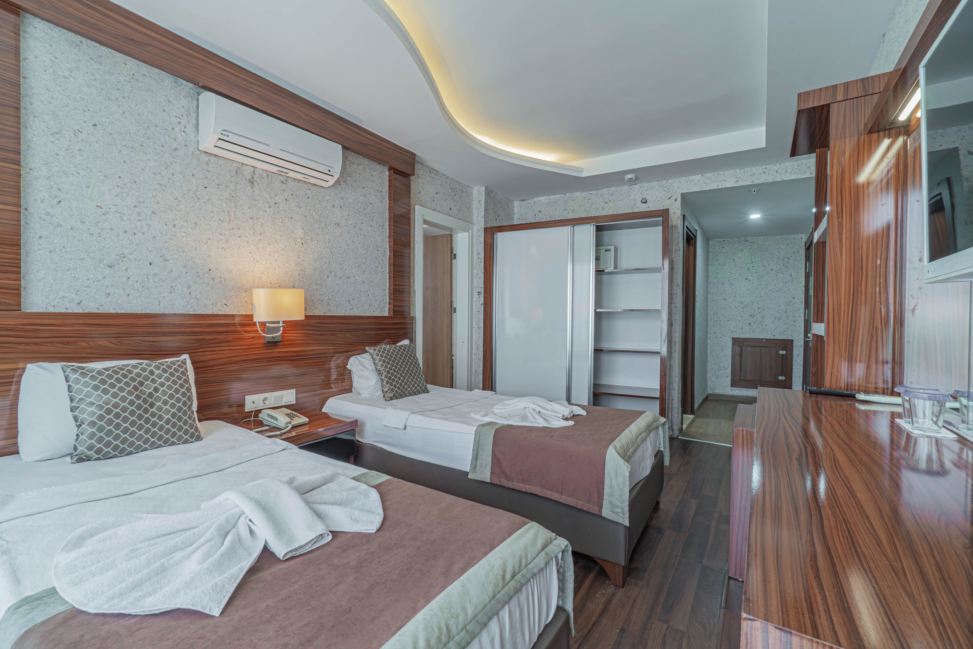 Ein Hotelzimmer mit zwei Betten, einem Holz-Kopfteil, einer Wand-Klimaanlage, einer Nachttischlampe und einem Kleiderschrank.