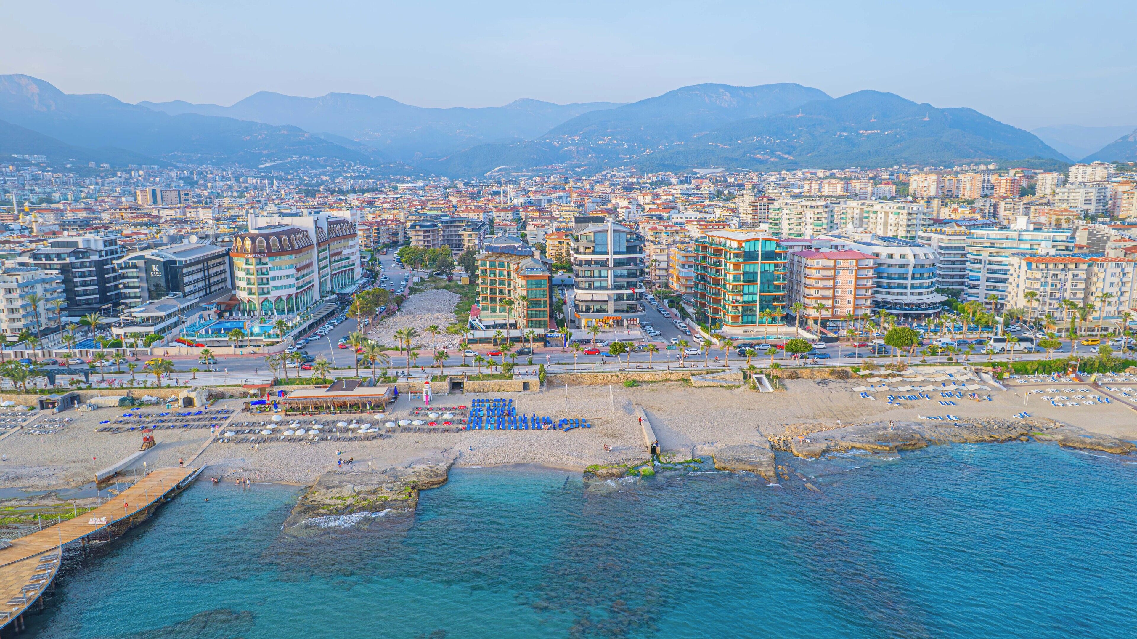 A coastal cityscape with modern buildings, a marina, and a beach area.