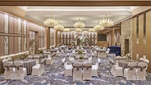 Une salle de banquet avec des tables rondes, des chaises blanches et des lustres.