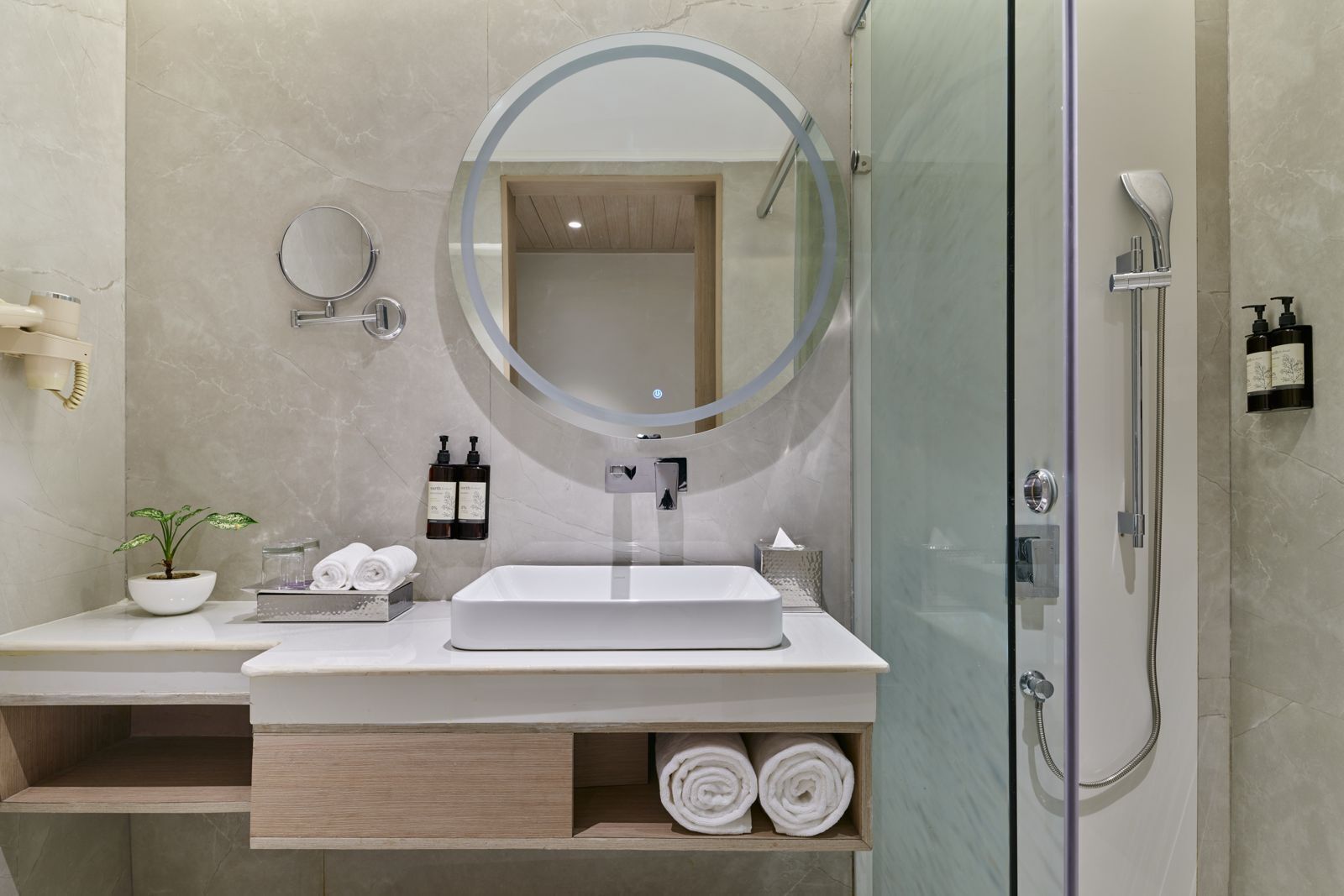 A modern bathroom with a large mirror, a sink, a shower, and a small plant.
