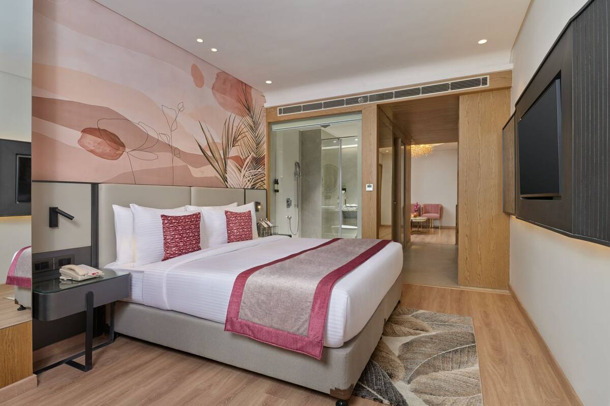 A modern hotel room with a large bed, a bedside table with a phone, a mirror, and a wall-mounted TV.