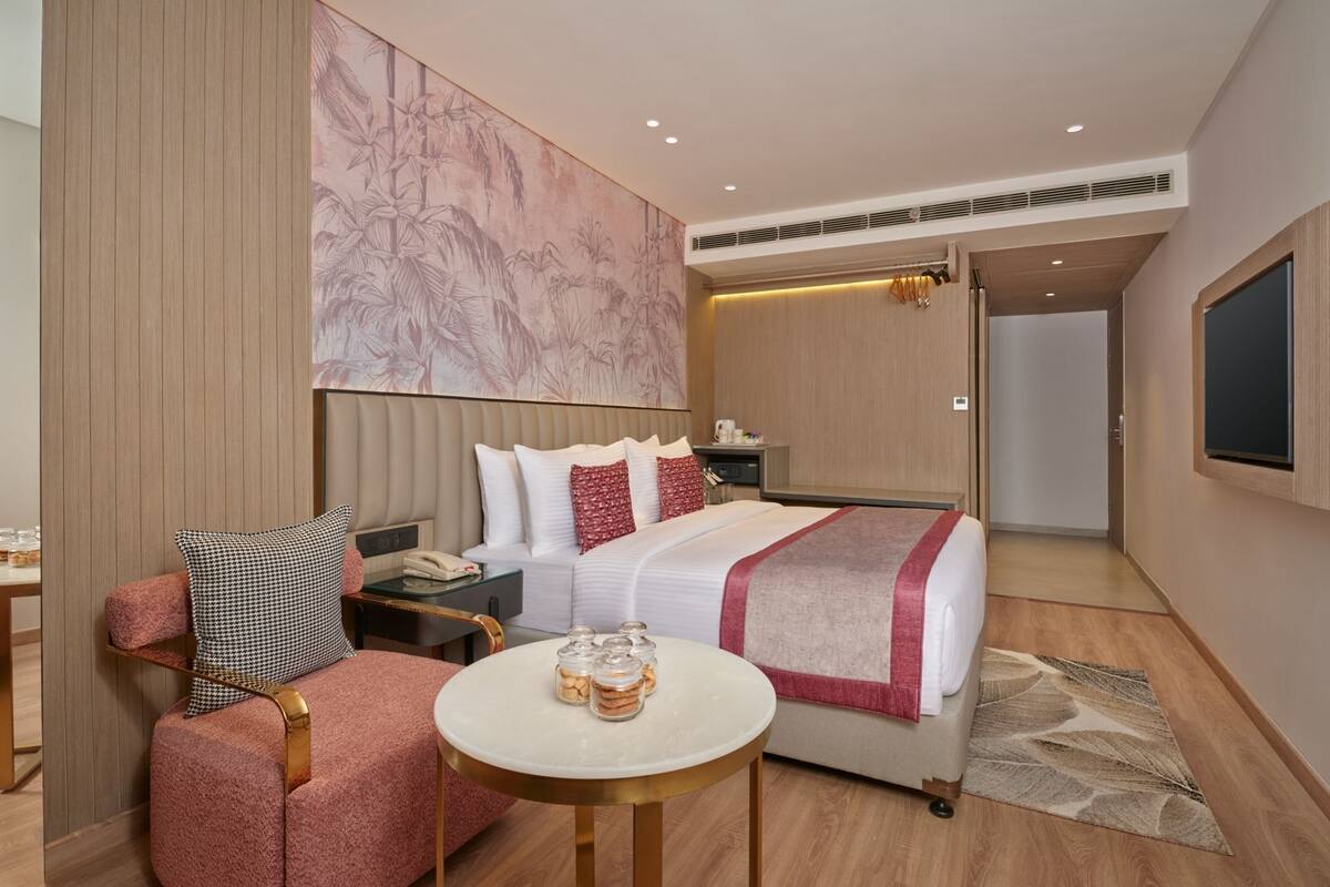 A hotel room with a bed, a desk, a chair, a small table, and a large wall mural.