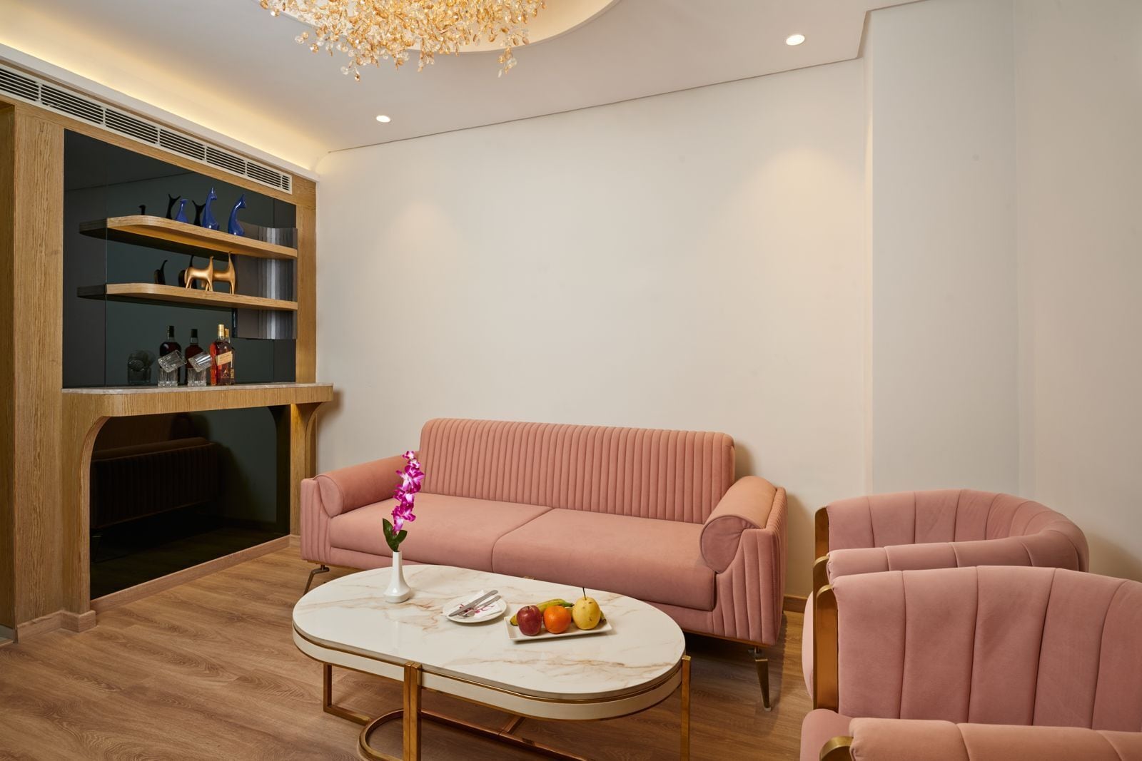 A modern living room with a pink sofa, a round coffee table, and a wooden shelving unit with bottles.