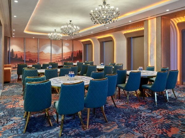 A conference room with round tables, teal upholstered chairs, and chandeliers. - Regenta Ranjit Avenue Amritsar (Amritsar)