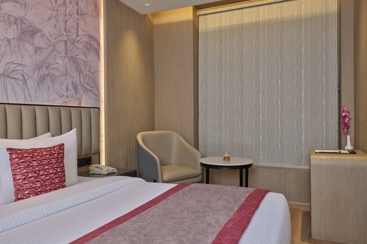 A hotel room with a large bed, a chair, a small table, and a vase with flowers.