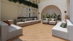 A spacious indoor seating area with multiple sofas and chairs, a tiled floor, and a large arched wall with greenery. - Ultimate Luxury Penthouse w Pool Marina Views (Dubai)