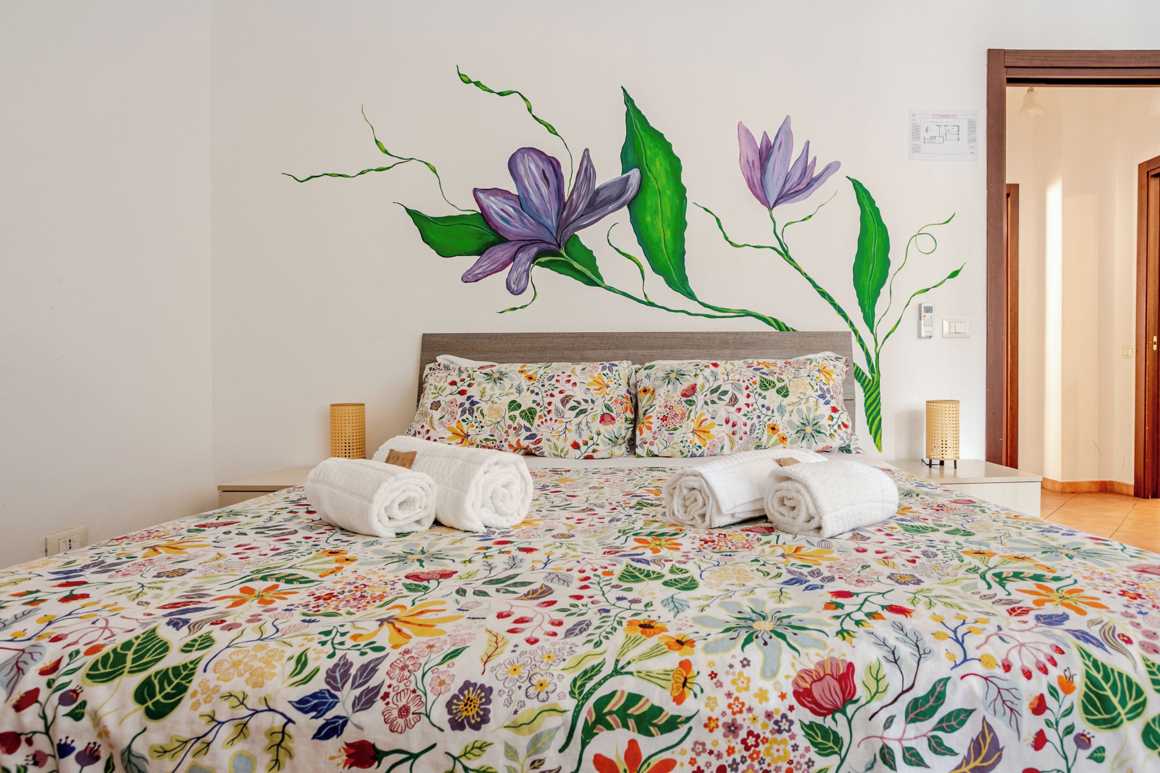 A hotel room with a bed, floral wall art, and a door.