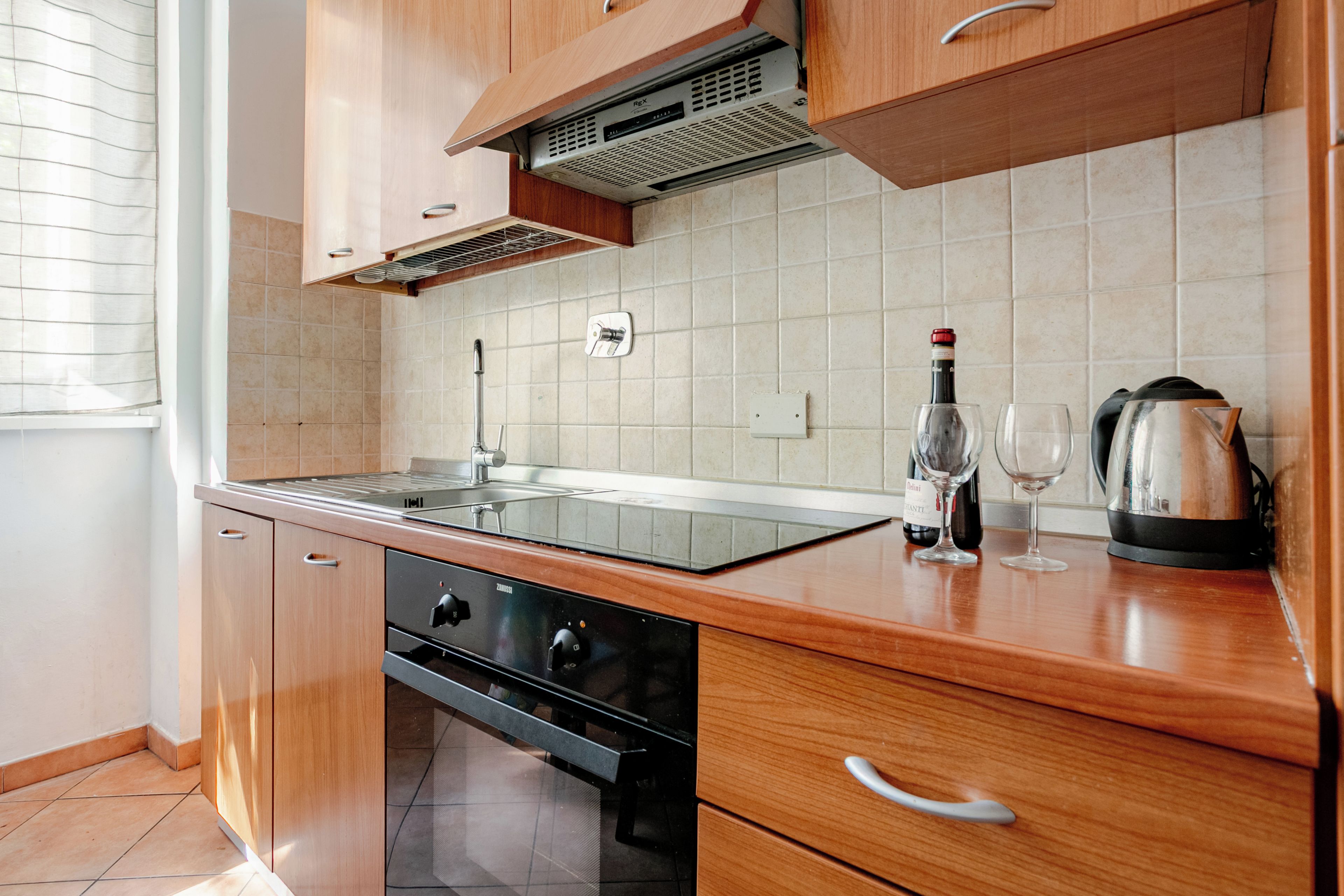 A modern kitchen with wooden cabinets, a built-in oven, and a stainless steel sink.