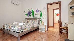 Quarto com cama, mesa de cabeceira, cadeira e porta que dá para outro espaço.
