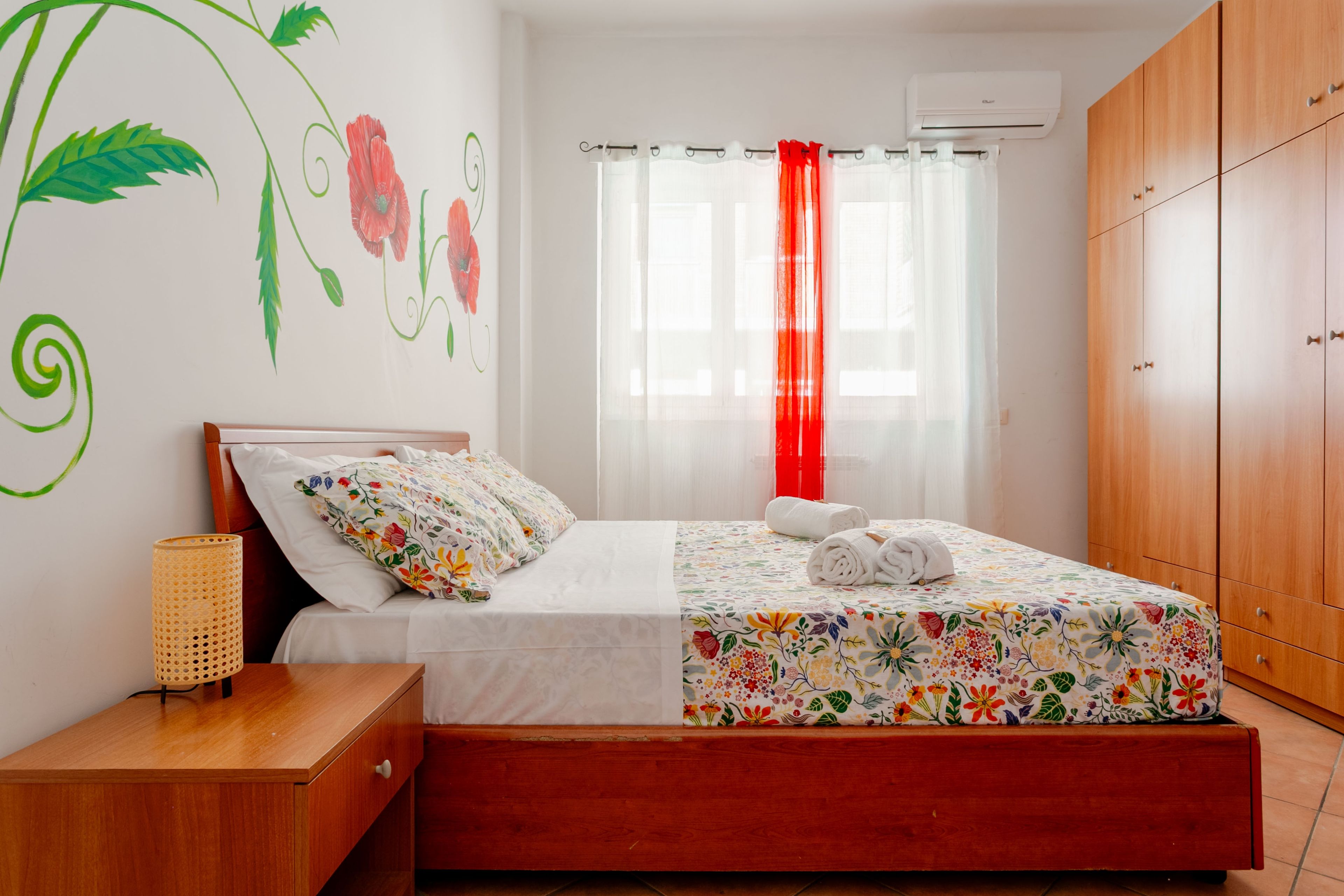 A bedroom with a bed, a nightstand, a wardrobe, and a window with curtains.