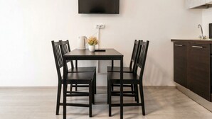 Une cuisine moderne avec une table à manger, des chaises, un téléviseur fixé au mur et un meuble de rangement.