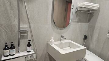 Une salle de bain moderne avec un lavabo rectangulaire, une douchette à main et des toilettes. On peut voir des bouteilles de shampoing et d’après-shampoing sur le bord du lavabo.