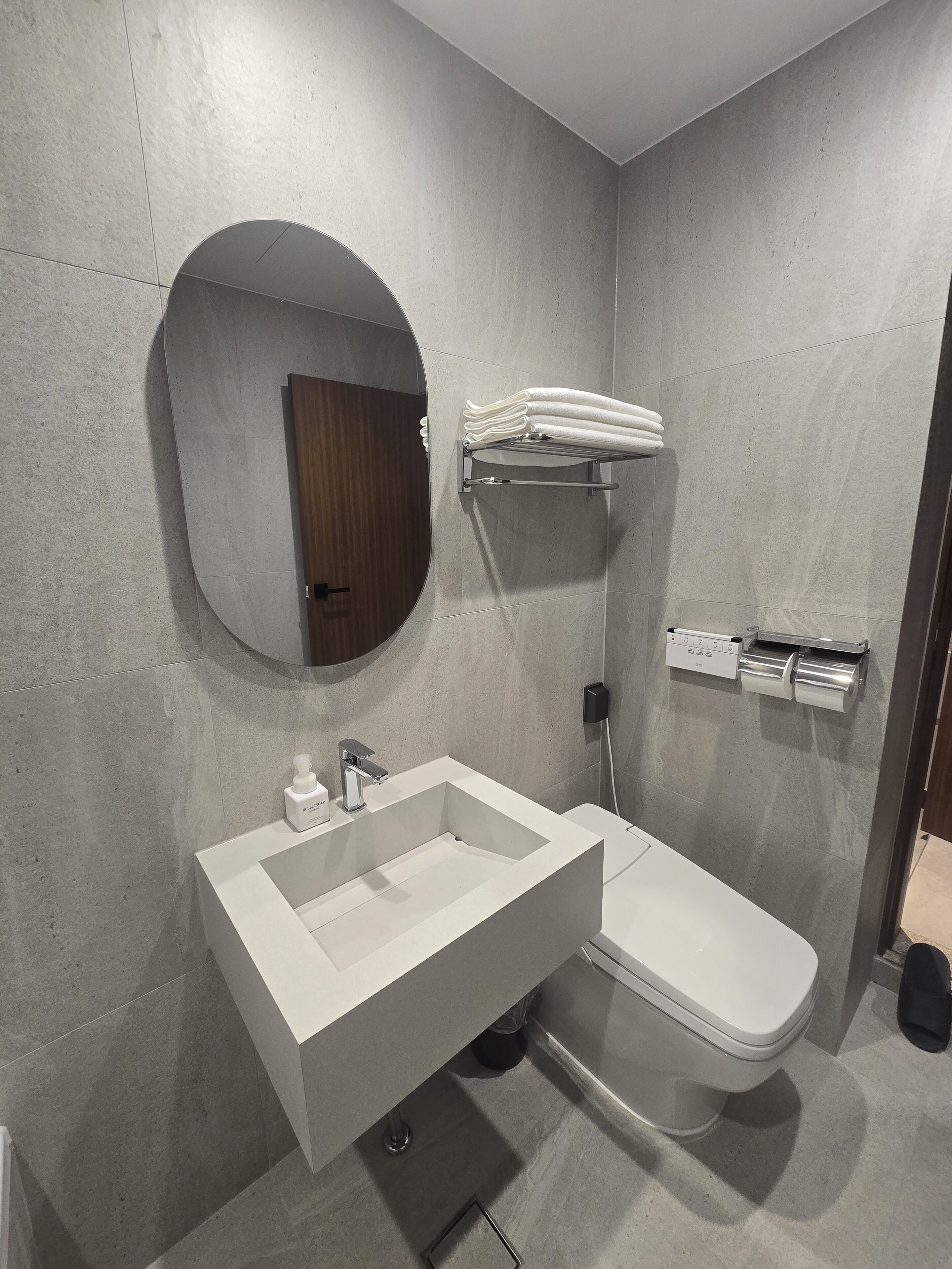 Een moderne badkamer met een rechthoekig wastafelmeubel, een toilet, een ronde spiegel en een handdoekrek.