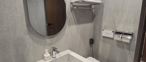 A modern bathroom with a rectangular sink, a toilet, a round mirror, and a towel rack.