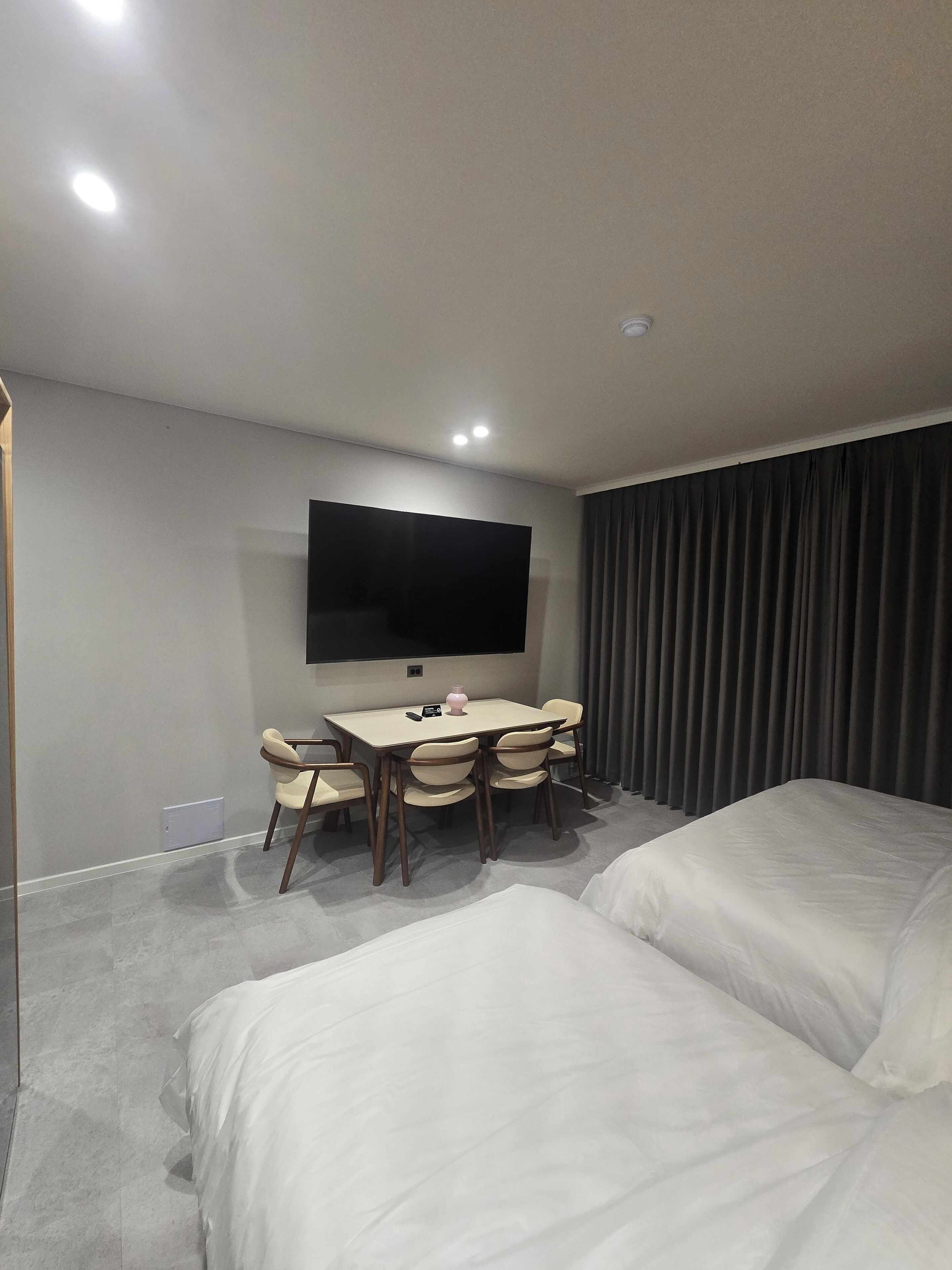 Une chambre d’hôtel avec deux lits, un téléviseur à écran plat fixé au mur, une petite table avec des chaises et une grande fenêtre avec des rideaux.