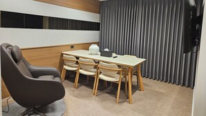 A modern meeting room with a wooden panel wall, a large grey curtain, a flat-screen TV, and a table with chairs. - Hound Hotel Tongyeong Jukrim (Tongyeong)