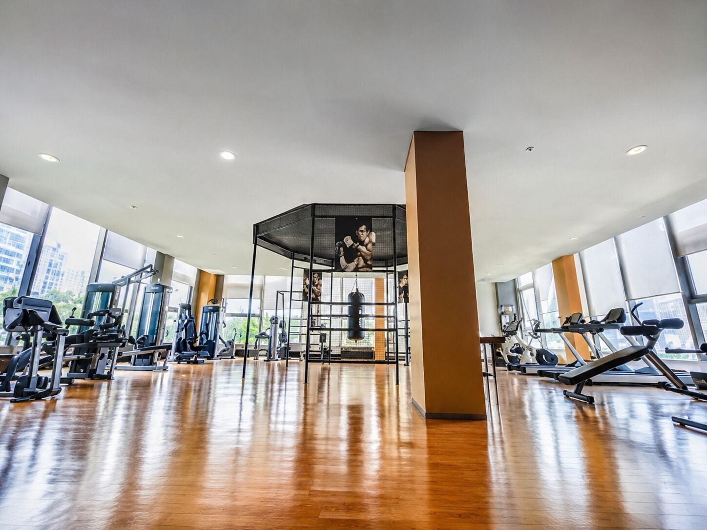 A gym with various exercise equipment, large windows, and a central pillar.