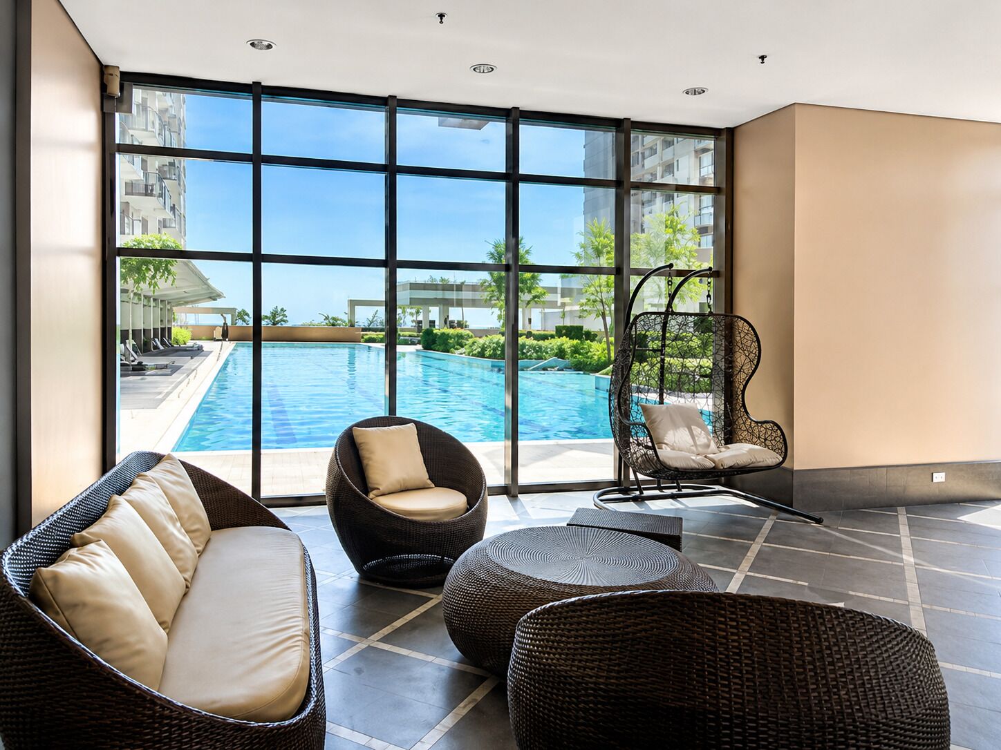 A modern indoor pool area with wicker furniture, large windows, and a view of the pool.