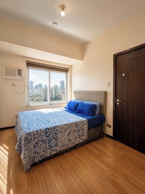 A bedroom with a large window, a bed with a patterned bedspread, a headboard, and a wooden floor. - LeMoon's Chill with beautiful view  (Pasay)
