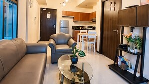 A modern living room with a glass coffee table, leather sofa, and a dining area with wooden cabinets and a kitchen in the background. - LeMoon's Chill with beautiful view  (Pasay)