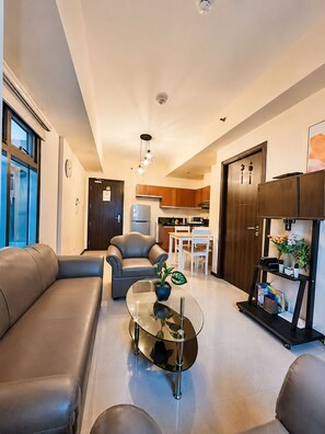 A modern living room with a glass coffee table, leather sofa, and a dining area with wooden cabinets and a kitchen in the background. - LeMoon's Chill with beautiful view  (Pasay)