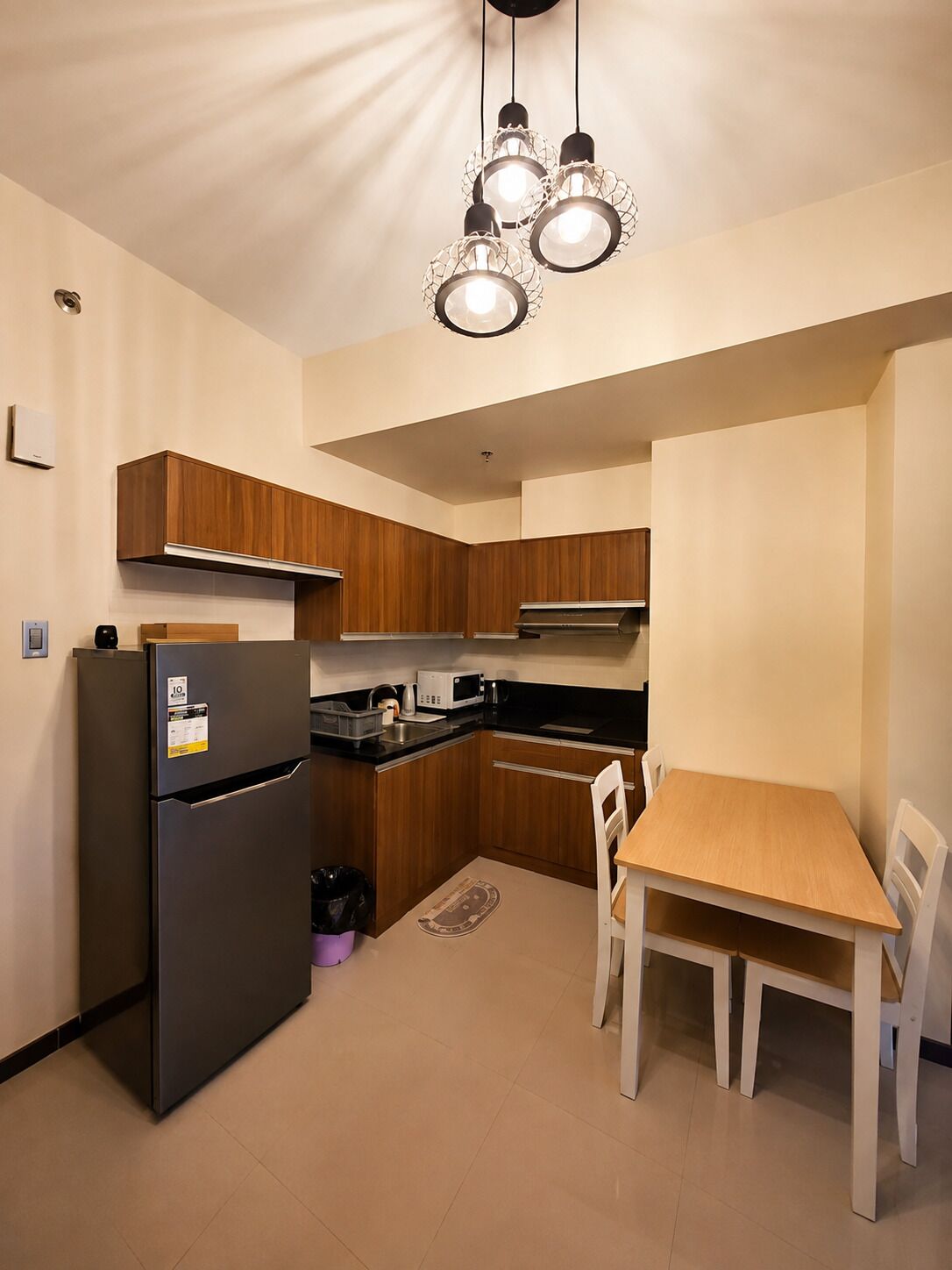 A compact kitchen with wooden cabinets, a black refrigerator, a microwave, and a dining table with chairs.