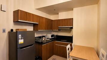 A compact kitchen with wooden cabinets, a black refrigerator, a microwave, and a dining table with chairs.