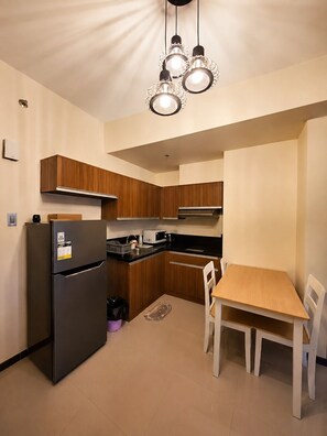 A compact kitchen with wooden cabinets, a black refrigerator, a microwave, and a dining table with chairs. - LeMoon's Chill with beautiful view  (Pasay)