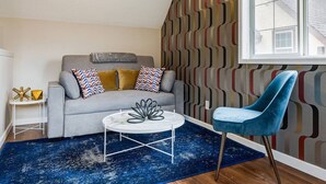 Una sala de estar moderna con un sofá gris, cojines estampados, un sillón azul, una mesa de centro blanca y una alfombra azul.