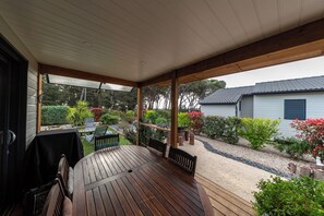Un porche cubierto con una mesa y sillas de madera, rodeado de un jardín con diversas plantas y un pequeño estanque.