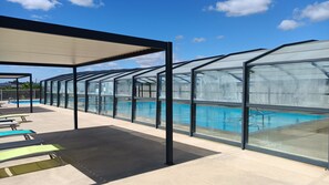 A covered swimming pool area with lounge chairs and a glass enclosure.