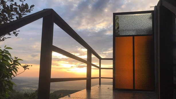 Una terraza de madera con un ventanal que ofrece vistas al atardecer.
