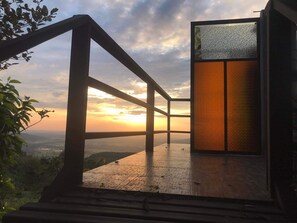 En træterrasse med glasdør, der giver udsigt over en solnedgang.