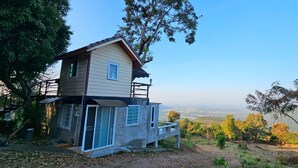 Una casa de dos pisos con balcón, rodeada de árboles y vistas al paisaje.