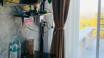 A room with a TV mounted on the wall, a desk with a lamp, two water bottles, and a bed with pillows.